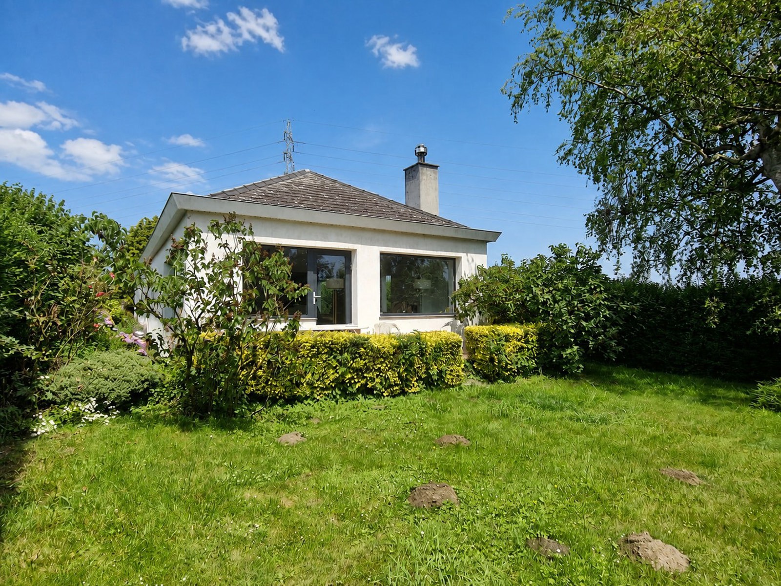 Vergezeld door de kat gaat u op ontdekking in deze gelijkvloerse woning, verscholen achter de garages. Zodra u onder de doorgang binnenkomt, leidt een pad u naar de ingang van de woning. Daar geeft een inkomhal toegang tot een ruime eetkamer. Met haar ingebouwde bibliotheek kunt u er volop genieten van uw boeken, terwijl u uw favoriete gerechten proeft of uw lectuur verderzet in de lichtrijke woonkamer die zich voor u opent.<br />
De volledig uitgeruste keuken, in de lengte ingericht, loopt door naar de wasplaats.<br />
Aan de andere zijde vervolledigen 2 comfortabele slaapkamers en een badkamer met inloopdouche en toilet het geheel.<br />
Buiten omringt de zorgvuldig aangelegde en beschutte tuin van 6 are de woning en versterkt hij haar rustige karakter. Elk raam biedt een rustgevend uitzicht op dit groene geheel.<br />
Technische aspecten: verwarming via een pelletkachel, houtinzet of accumulatiesysteem, conforme elektriciteit, nieuwe ramen PVC met dubbele beglazing, gevel in crepi met isolatie.<br />
EPC D (20260614012464)<br />
Prijs onder voorbehoud van aanvaarding door de eigenaars.